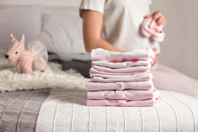 Pile of baby clothes and pregnant woman on bed