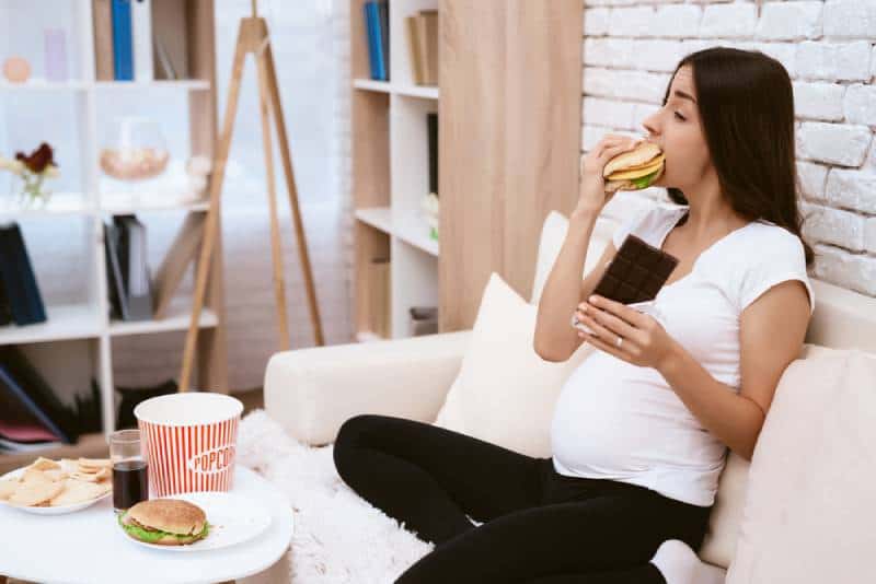 pregnant woman eating a hamburger and chocolate