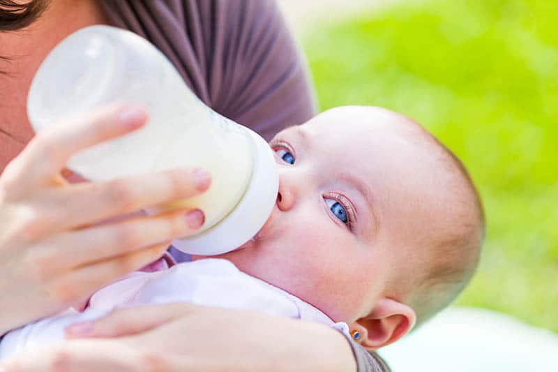 Baby with blue eyes drinking milk from bottle