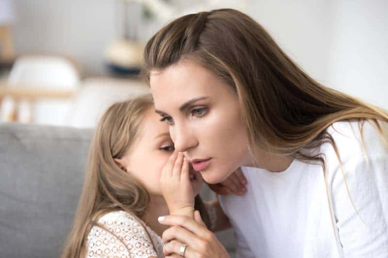 mother carefully listens to child girl whispering in ear
