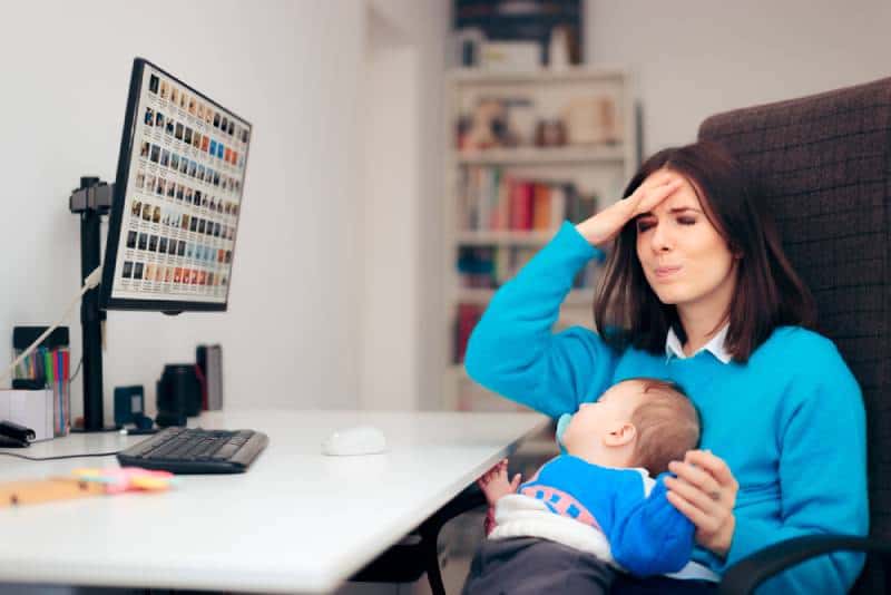 Forgetful mother holding baby in her lap at the desk and starting to panic