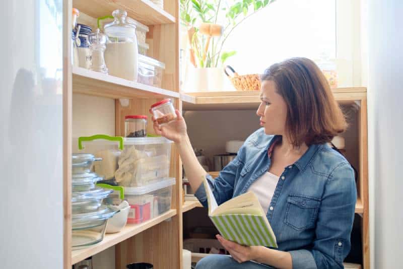 Woman in pantry with groceries, wooden shelf for food storage in kitchen