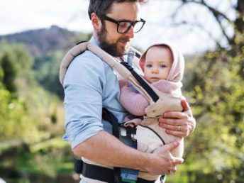 A father with his toddler daughter in a baby carrier outside on a spring walk