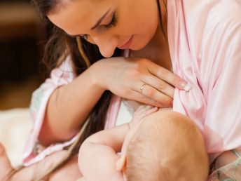 Young mum in pink nursing nightwear nurses the child on on the house bed