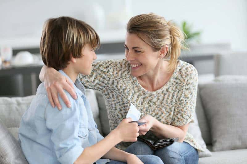 Mother giving money to adolescent for reward while they are sitting on a couch
