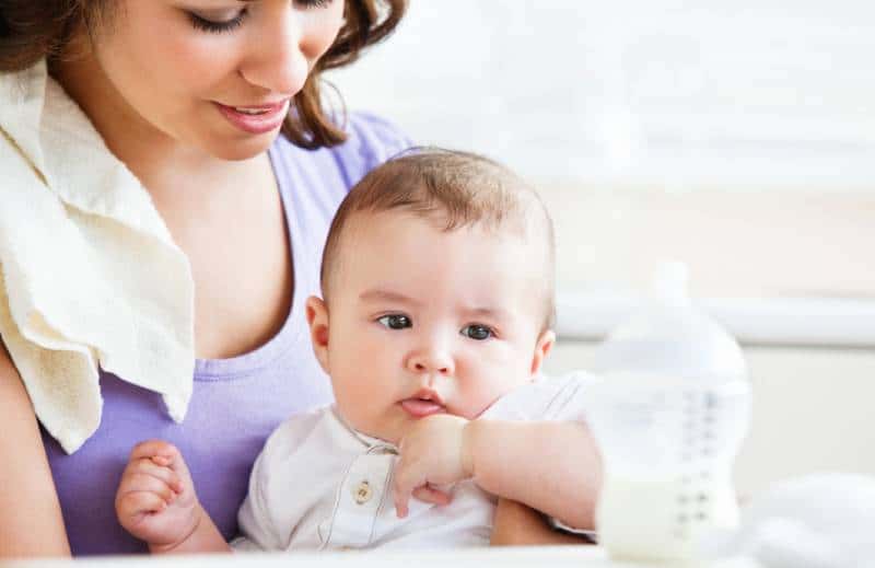 Mother holding baby that's looking at the milk bottle on the table