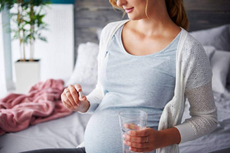 Young pregnant woman taking capsule in her home