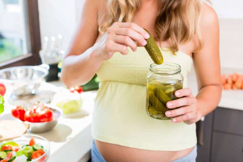 Pregnant woman with pickles and lots of food in the kitchen