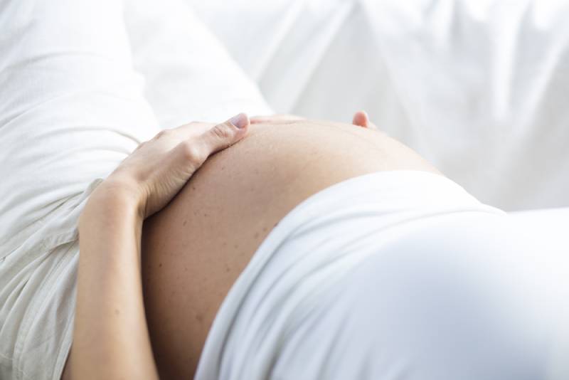 Pregnnat woman in white lying and holding her belly