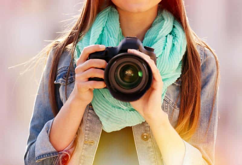 Young photographer in denim jacket and green scarf taking photos outside