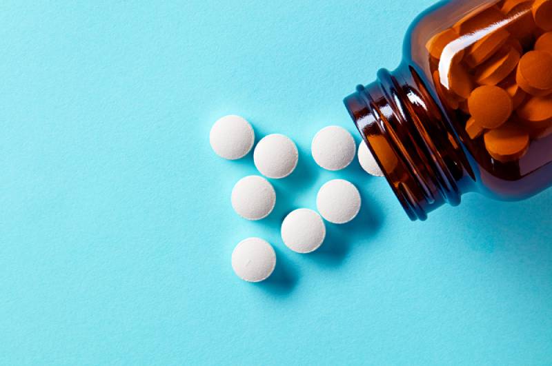 White medical pills and tablets spilling out of a drug bottle on a blue background