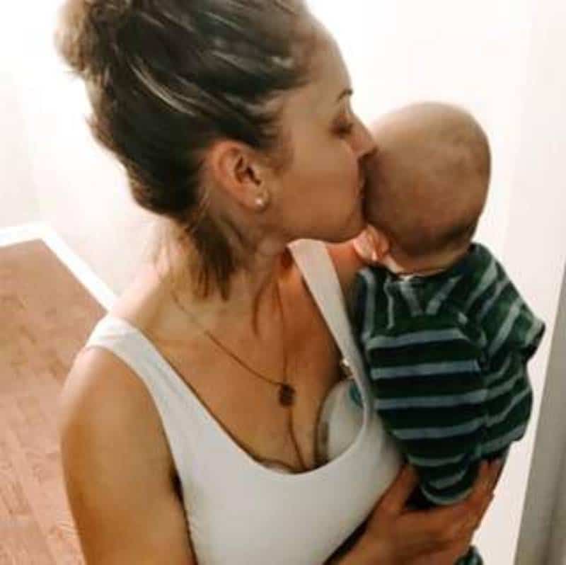 Mom in white shirt holding a baby while pumping indoor