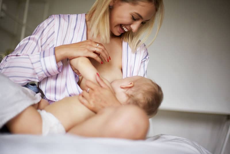 smiling young mother breastfeeding baby who is biting her nipple