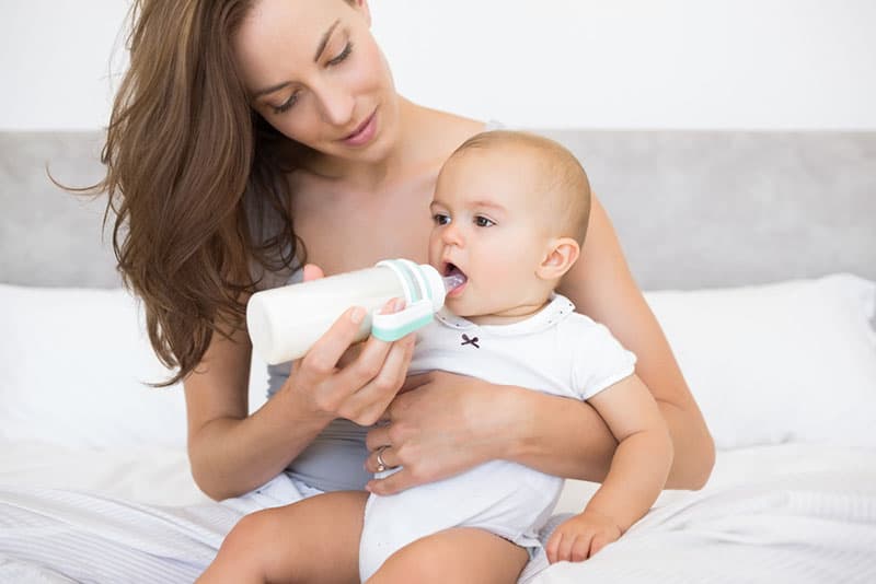 beautiful mother bottle feeding her baby on bed