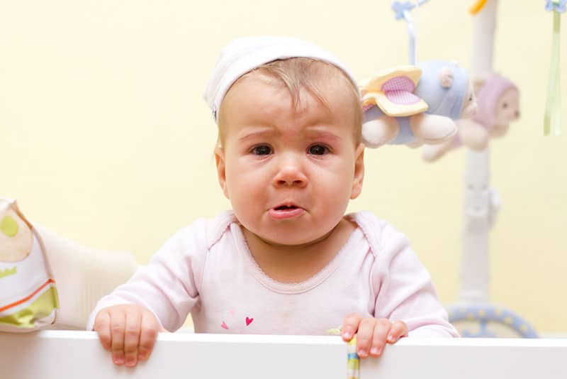 cute baby crying and standing in the bed