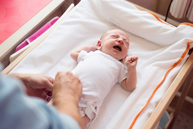 mother trying to changer diaper to crying baby