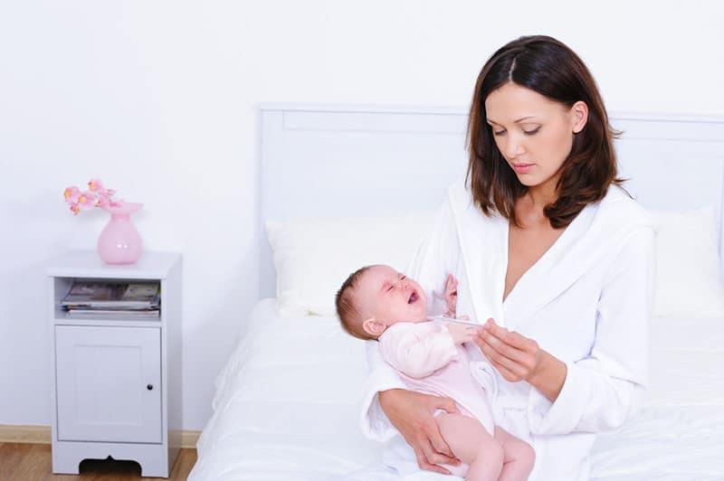 worried mother measuring temperature to her little son