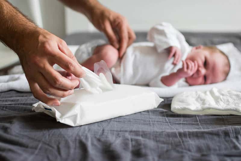 Vater wechselt die Windel des Neugeborenen und nimmt ein feuchtes Tuch, um das Baby zu reinigen