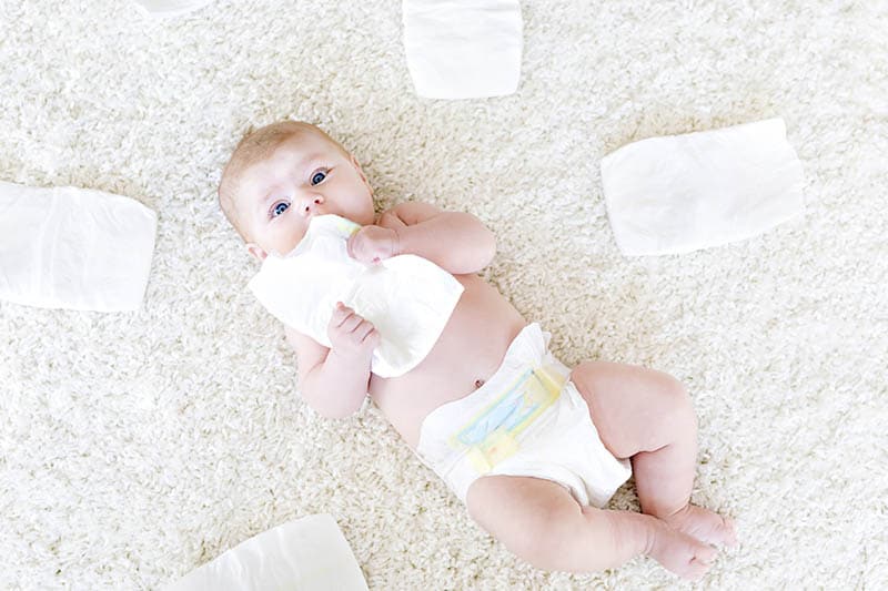 adorable baby boy lying on the floor full of diapers around him and in his hands