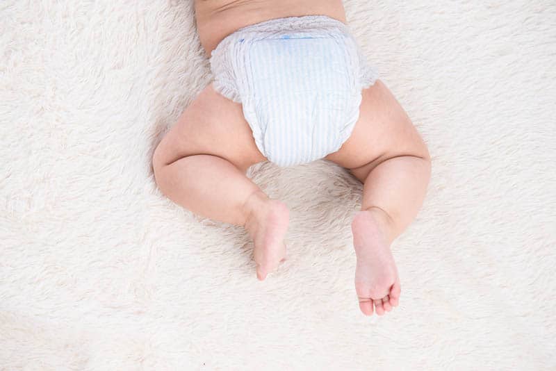 bebê vestindo fraldas deitado no cobertor branco 