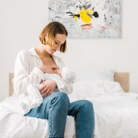young mother breastfeeding baby on bed