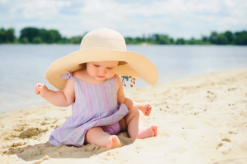 cute baby girl wearing big hat and playing on the beach sand