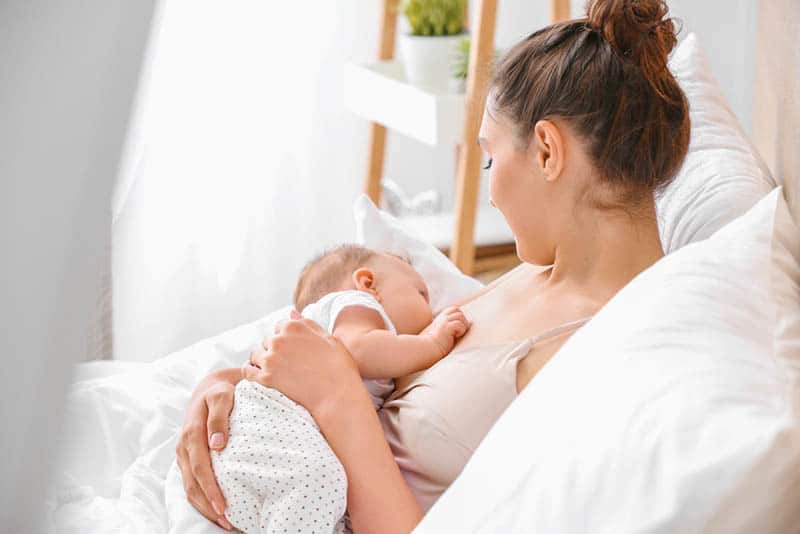 young woman breastfeeding baby in the bed