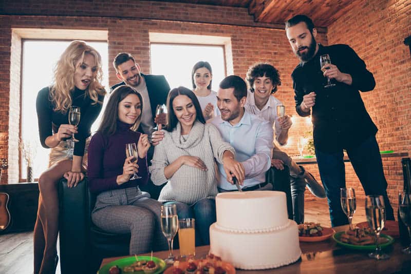 pregnant woman and her husband cutting cake with friends on the baby shower party