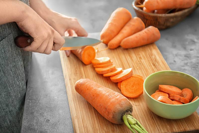woman cutting carrot on the wooden board and putting it into bowl