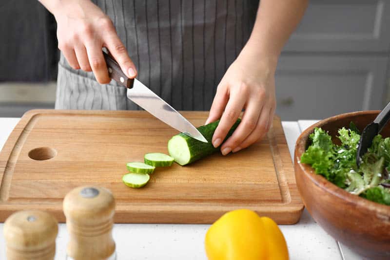 woman cutting fresh cucumber on the wooden board in the kitchen