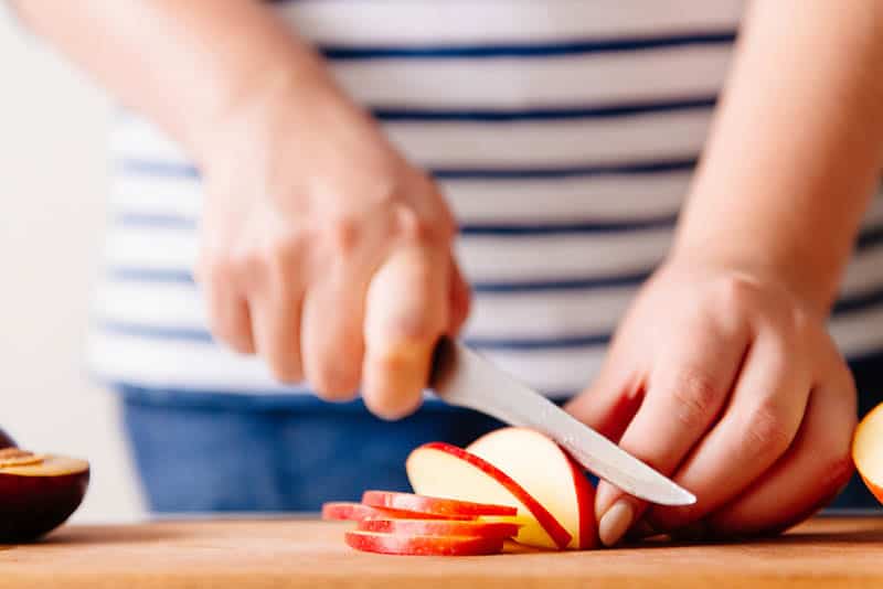 woman cutting red apple on the wooden cutting board at home