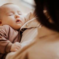 young mother holding sweet sleeping baby boy in arms