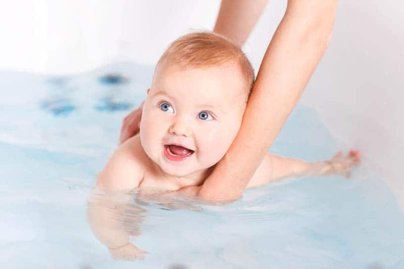 entzückendes Baby mit blauen Augen, das von der Mutter gebadet wird