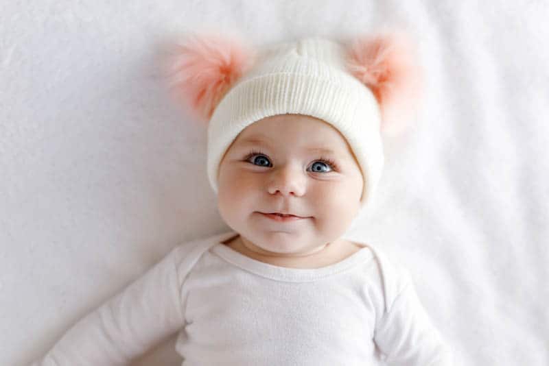 baby girl wearing hat with interesting bobbles on the bed