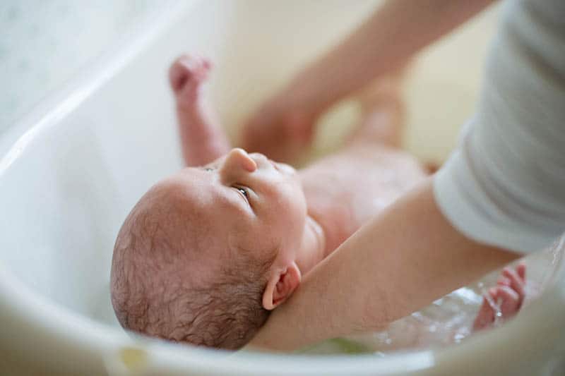 mor, der bader sin baby søn i en plastbat derhjemme