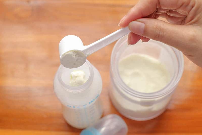 mother getting milk powder to a baby bottle on the table