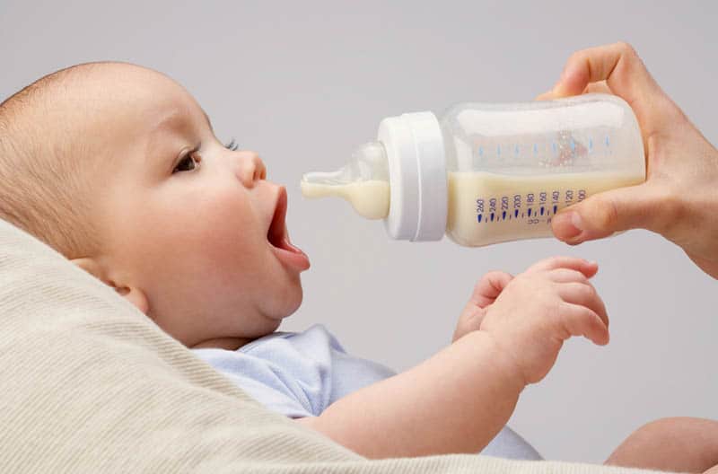 mother giving milk bottle to her baby at home