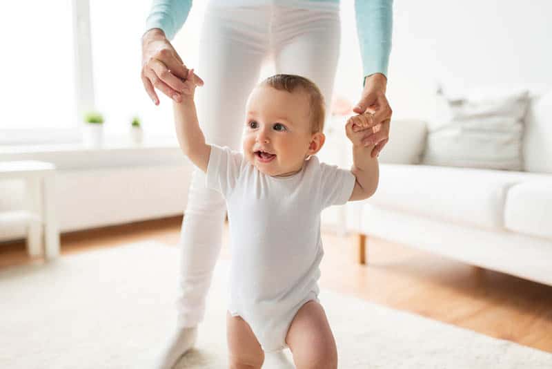 mother holding baby for hands while teaching him to walk