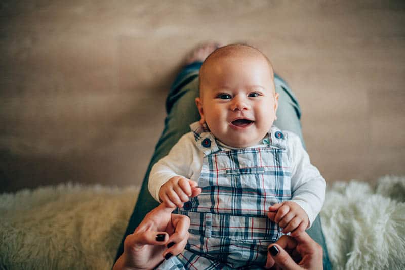 mother holding cute smiling baby on her legs