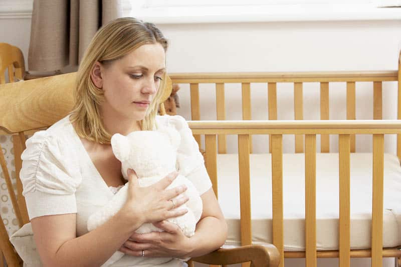 sad mother sitting in nursery and hugging teddy bear