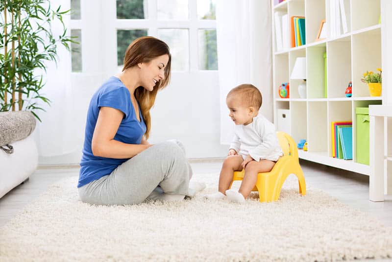 smiling mother learning baby how to sit on a potty