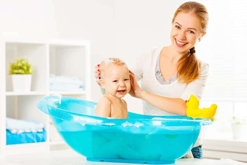 sorridente madre in posa con bambino felice in vasca a casa