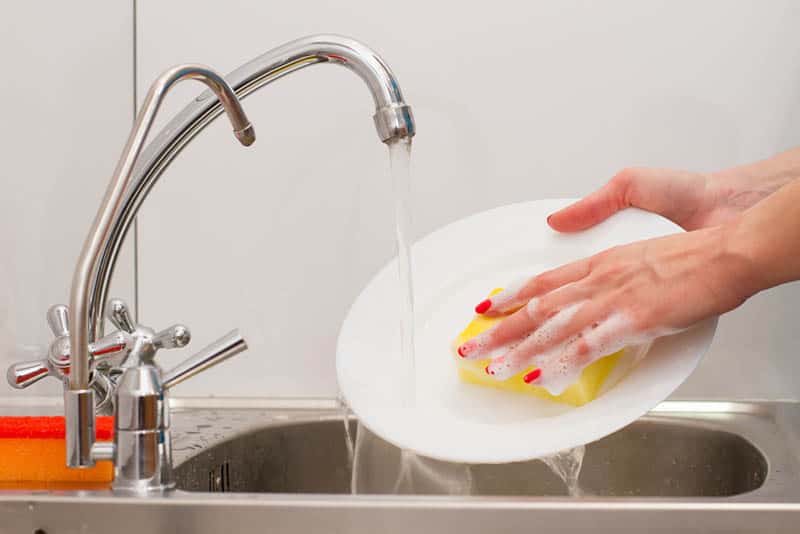 woman with red nail polish washing plate in the sink 