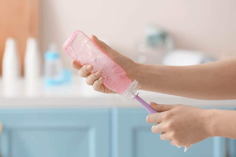 young mother cleaning pink baby bottle with brush at home