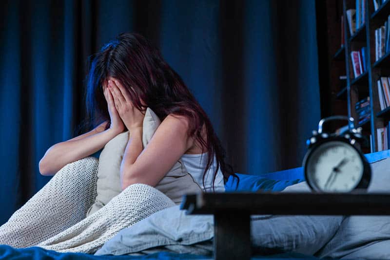 young woman crying in hands after nightmare in bed