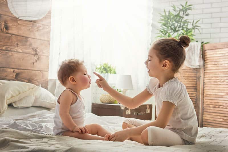cute little girl playing with her baby brother on the bed