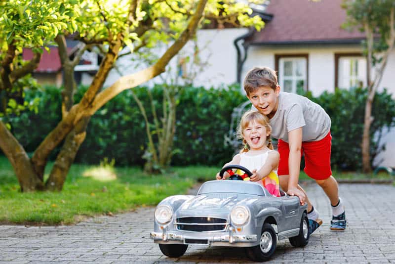 older brother playing with his sister in a car toy outdoor
