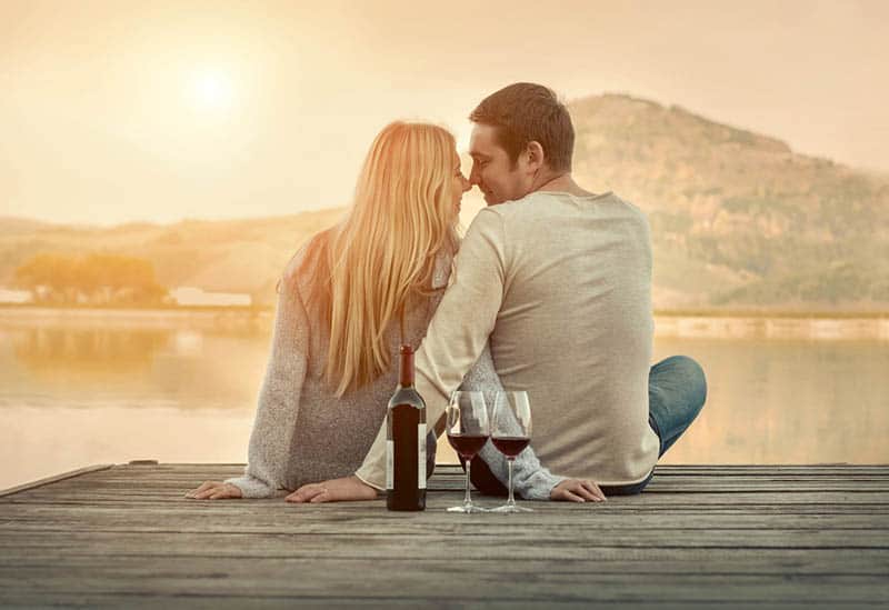 romantic couple sitting on the pier with bottle of wine