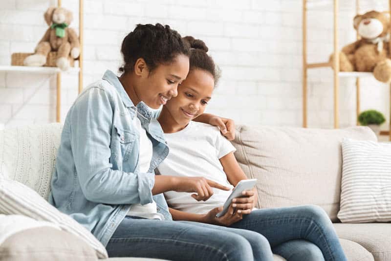 two sisters sitting on the couch looking at mobile phone