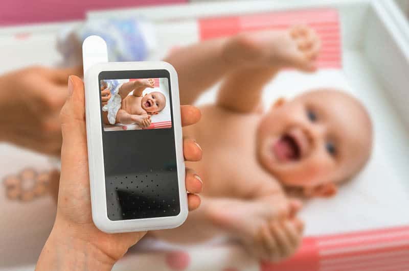 Hand of mother is holding baby monitor camera for safety of her cute baby